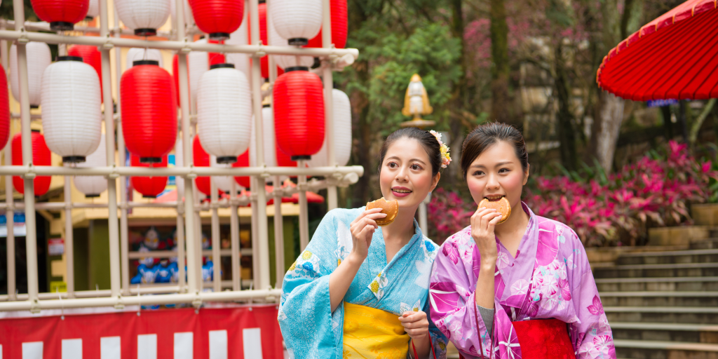8 Dates to Celebrate in February - This photo features two ladies who are wearing Kimonos and eating Dorayaki. There are lanterns in the background.