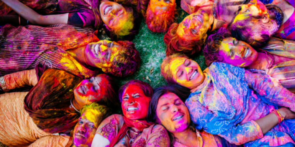 8 Dates to Celebrate in March: This is a photo of the Holi Festival. There are people laying on the ground with their heads together, covered in bright colours.