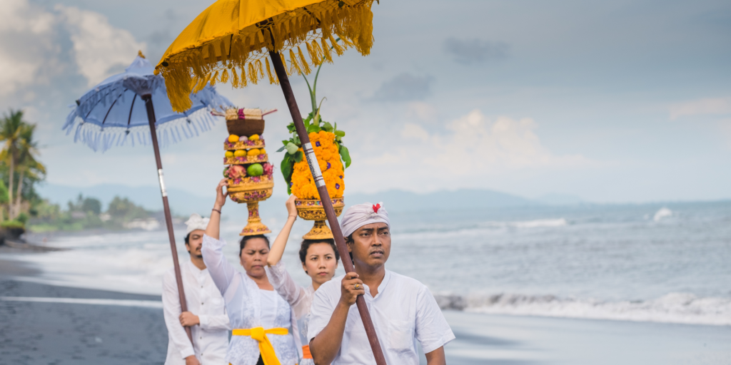 8 Dates to Celebrate in March: This is a photo of four Indonesian people carrying umbrellas and fruit.