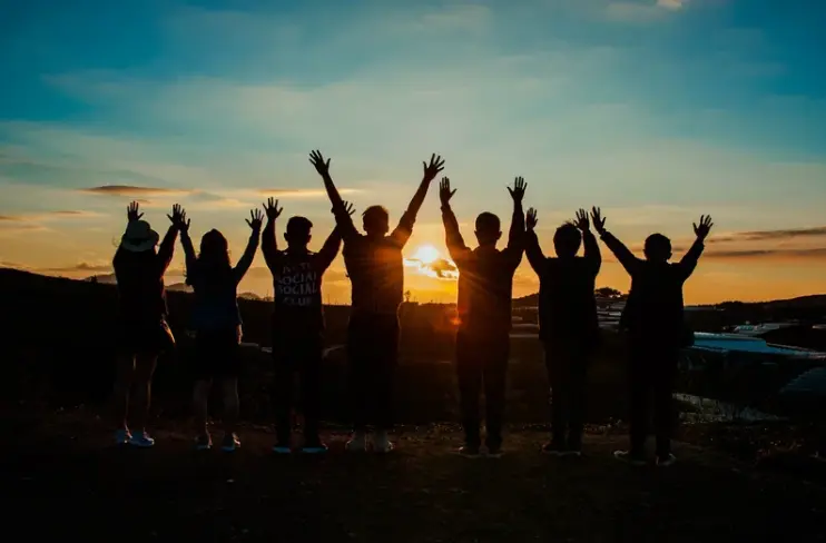 Photo of people silhouetted against sun with hands raised, symbolising harmony